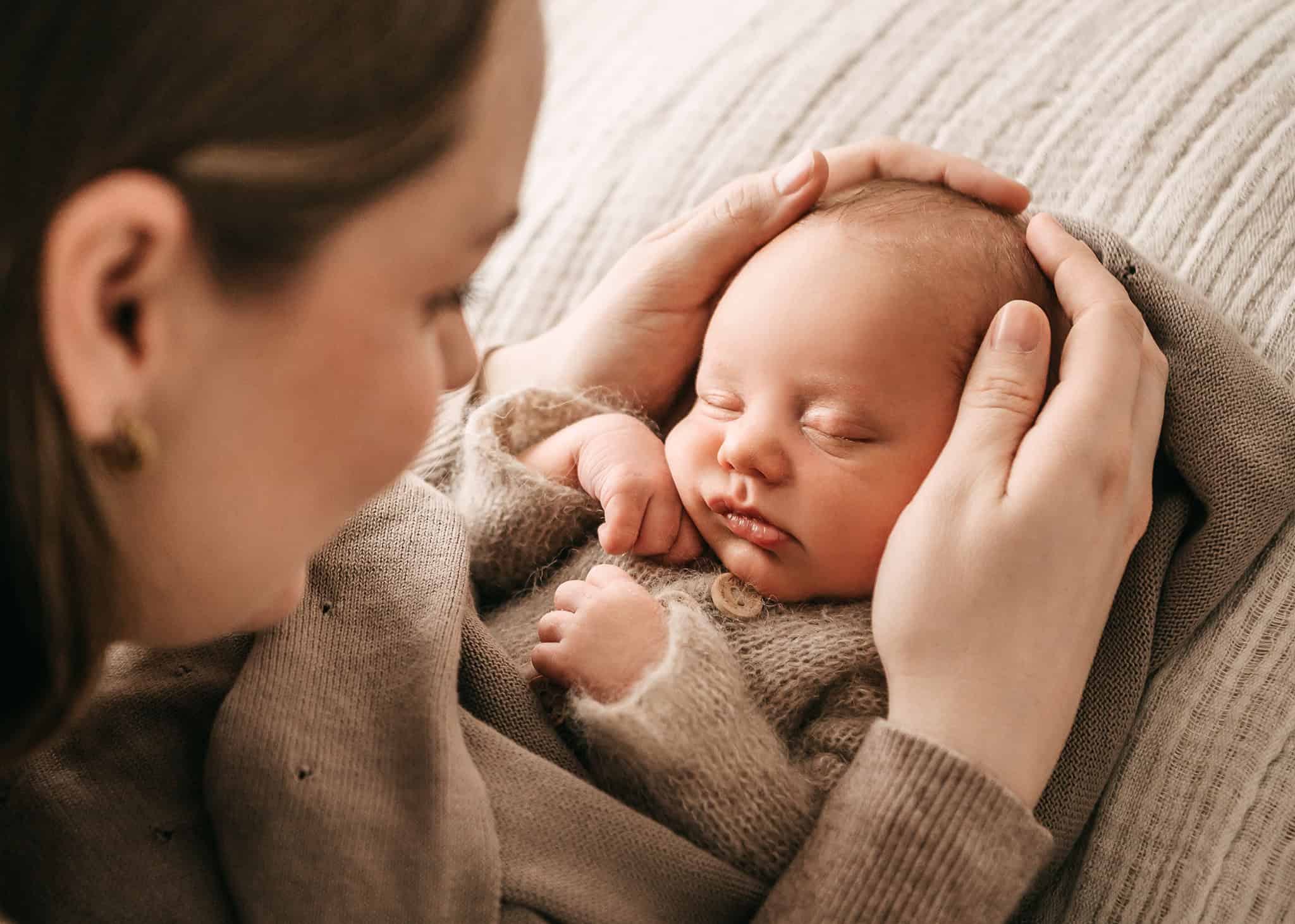 Mother cradling her sleeping newborn baby, resting in a cozy knitted blanket and sweater.