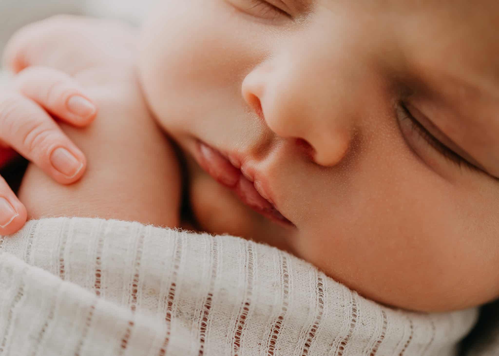 Close-up of a sleeping infant with a hand resting near the cheek, wearing a white knit garment